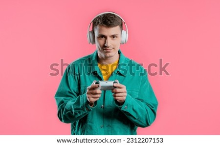 Handsome young man playing video exciting game on Tv with joystick isolated on pink studio background. Using modern technology.