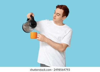 Handsome young man pouring hot water from modern electric kettle into mug on blue background - Powered by Shutterstock