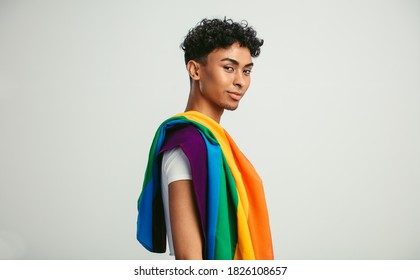 Handsome young man with pride movement LGBT Rainbow flag on shoulder against white background. Man with a gay pride flag looking at camera. - Powered by Shutterstock