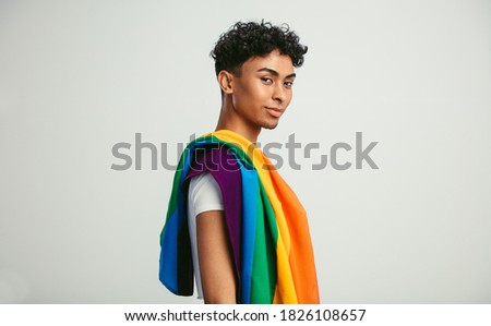 Handsome young man with pride movement LGBT Rainbow flag on shoulder against white background. Man with a gay pride flag looking at camera.