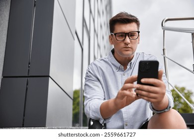 Handsome young man with prosthetic leg looks down at his smartphone while seated outdoors. - Powered by Shutterstock