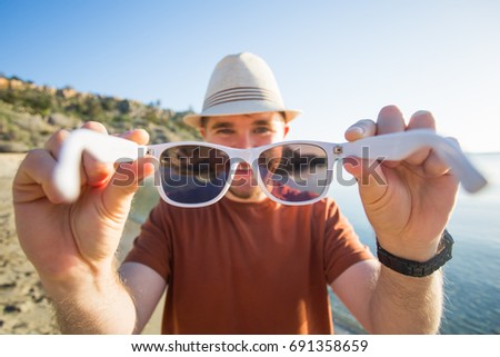 Handsome young man puts on camera sunglasses on the beach. Travel, fun, summer and vacation concept