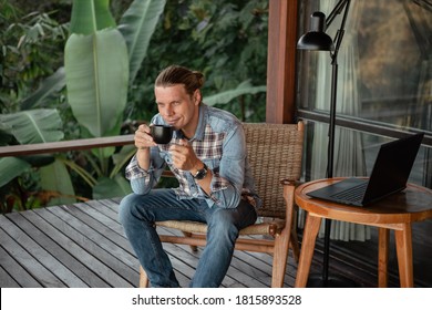 Handsome Young Man Relaxing And Working On Laptop Computer At Home Balcony With Tropical Nature, Drink Coffee