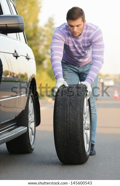 Handsome\
young man rolling a spare wheel using\
gloves