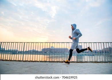 A handsome young man running in the sunset next to a fence on the riverside