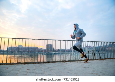 A Handsome Young Man Running In The Sunset Next To A Fence On The Riverside
