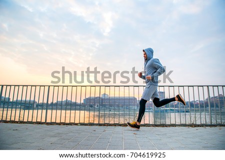 A handsome young man running in the sunset next to a fence on the riverside
