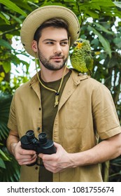 Handsome Young Man In Safari Suit Looking At Parrot On Shoulder In Jungle