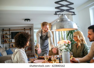 Handsome Young Man Serving Food To Friends At Home. 