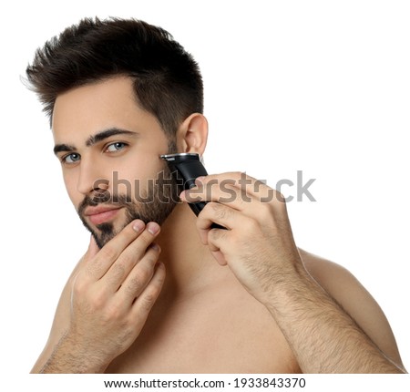 Handsome young man shaving with electric trimmer on white background