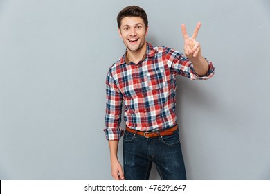 Handsome Young Man Showing Victory Fingers Sign Over Gray Background