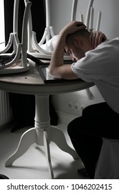 Handsome Young Man Sit Alone Sad In White Apartment, Hold Head With Hands And Look Into The Mirror On Table