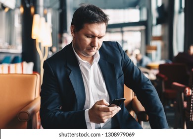 Handsome young man sitting in a bar, using his mobile phone to read the latest business news and stay informed. - Shutterstock ID 1308979069