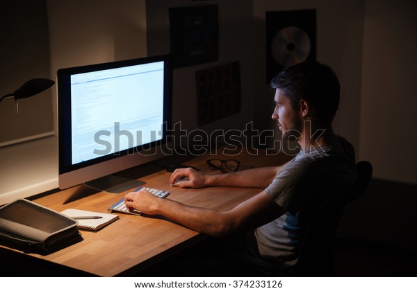 暗い部屋に座ってパソコンを使うハンサムな若者 の写真素材 今すぐ編集
