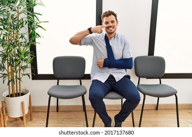 Handsome Young Man Sitting At Doctor Waiting Room With Arm Injury Pointing With Hand Finger To Face And Nose, Smiling Cheerful. Beauty Concept 