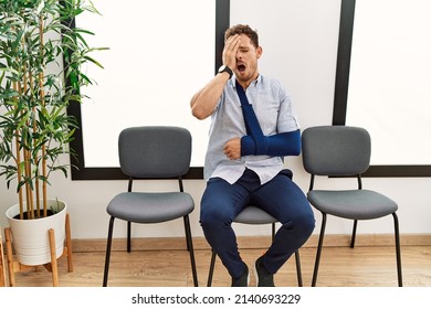 Handsome young man sitting at doctor waiting room with arm injury yawning tired covering half face, eye and mouth with hand. face hurts in pain. 
