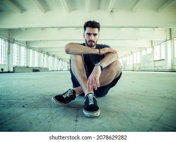 Handsome Young Man Sitting On The Floor In Empty Warehouse