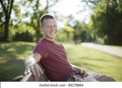 Handsome Young Man Sitting On A Bench Smiling. Candid.