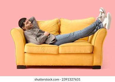 Handsome young man sleeping on yellow sofa against pink background - Powered by Shutterstock