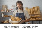 Handsome young man smiling in a bakery while holding a basket of assorted fresh bread with shelves of baked goods in the background