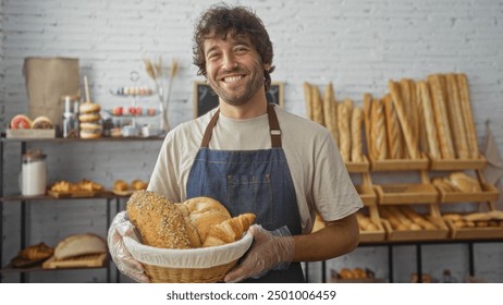 Handsome young man smiling in a bakery while holding a basket of assorted fresh bread with shelves of baked goods in the background - Powered by Shutterstock