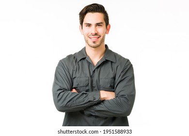 Handsome young man smiling while standing in front of a white background. Hispanic handyman with his arms crossed and making eye contact - Shutterstock ID 1951588933