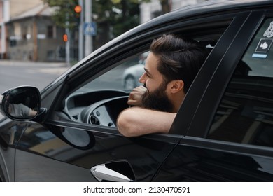 Handsome young man smiling while driving a car. Happy male driver smiling while sitting in a car with open front window.