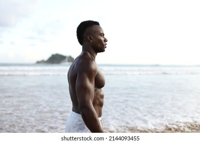 Handsome Young Man Standing On A Ocean Beach.shirtless Wearing Boxer Shorts, Showing Muscular Fit Body.Perfect Body.Looking Away.Ocean Background