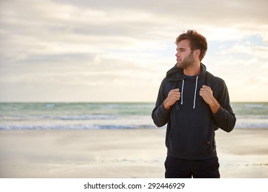 Handsome young man standing on a beach early in the morning looking away contemplatively - Powered by Shutterstock