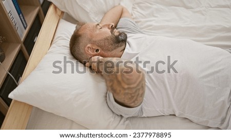 Handsome young man suffering from excruciating cervical pain, lying in bed touching neck with agony in his bedroom