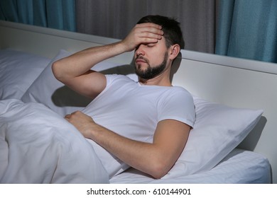 Handsome young man suffering from headache while lying in bed at night