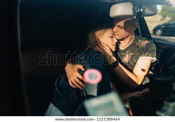 Handsome young man in\
summer clothes embracing delicately beautiful relaxed blond woman\
covered with jeans jacket leaning on him sitting on front seat of\
car with closed eyes