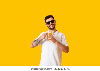 Handsome young man in sunglasses with glass of beer on yellow background