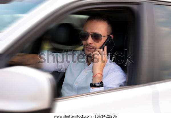 handsome young man in sunglasses\
talking on the phone while driving car breaking safety\
rules.