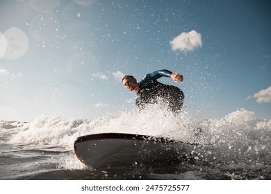 Handsome young man surfer in a wetsuit was waiting for a passing wave and stood on a surfboard, spray is flying around - Powered by Shutterstock