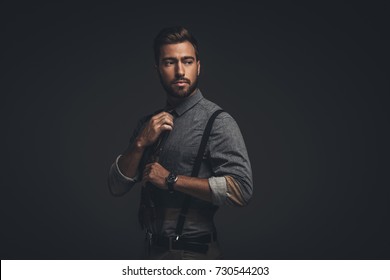 Handsome Young Man In Suspenders Adjusting His Tie