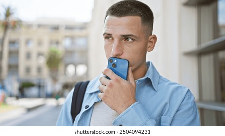 Handsome young man talking on smartphone on urban street, wearing casual business attire with backpack - Powered by Shutterstock