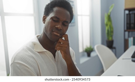 Handsome young man thinking deeply in a modern office setting with indoor plants and bright natural light through large windows - Powered by Shutterstock