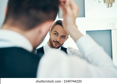 Handsome Young Man Touching His Hair With Hand And Smiling While Standing In Front Of The Mirror