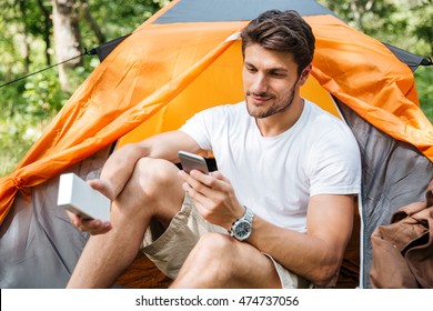 Handsome Young Man Tourist Using Cell Phone And Portable Mini Speaker In Touristic Tent