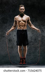 Handsome Young Man Training With His Skipping Rope. Photo Of Sporty Muscular Man With Perfect Body On Dark Background. Best Cardio Workout