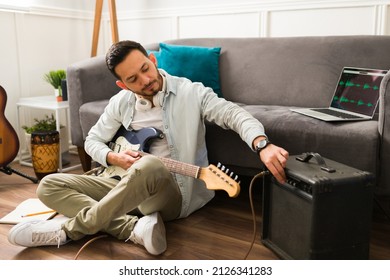 Handsome young man using an amplifier while playing the electric guitar at home 