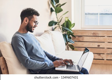 Schöner junger Mann mit Laptop-Computer zu Hause. Studentinnen ruhen in seinem Zimmer. Hausarbeit oder Studium, Freiberufler Begriff