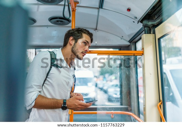 Handsome young\
man using smartphone in bus.  Handsome man standing in city bus and\
typing a message on the phone. Businessman commuting to work by bus\
and working with a\
smartphone