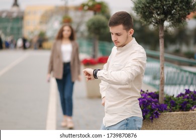 Handsome Young Man Waiting For Girlfriend Outdoors And Looking On The Watch. Girl Is Coming To Her Boyfriend