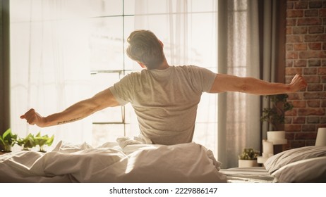 Handsome Young Man Waking up in the Morning, Stretches and Gets Out of Bed, Sun Shines From the Apartment Window in Bedroom, He is Ready for Business Opportunities, Achievements, Adventures