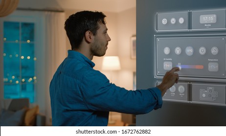 Handsome Young Man Walks Over to a Refrigerator. He is Changing Temperature on Smart Fridge Screen at Home. Cozy Kitchen Evening.