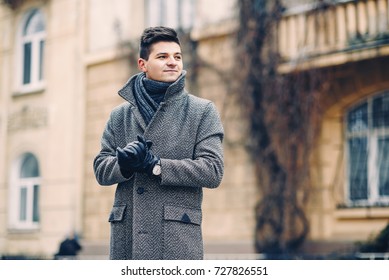 A Handsome Young Man In A Warm Coat, Leather Gloves With A Watch On A City Walk