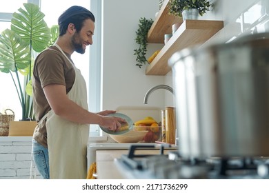 Handsome young man washing dishes at the domestic kitchen - Powered by Shutterstock