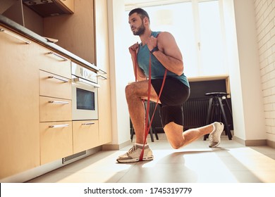 Handsome Young Man Watching Online Workout On Laptop And Using Elastic Rope During Morning Training